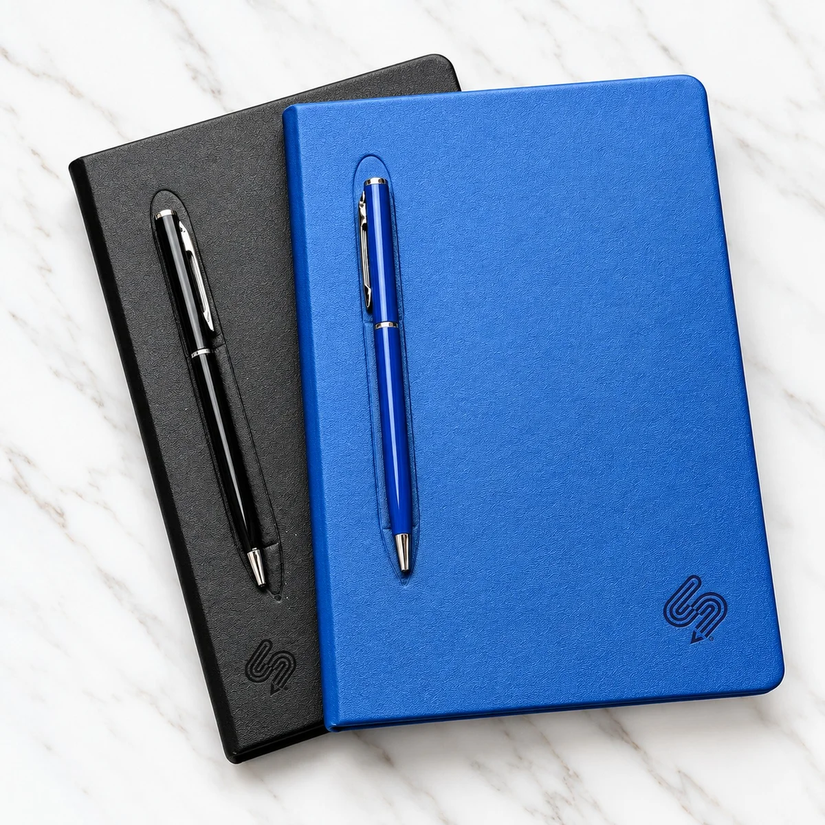 Blue and black Ventura Visuals branded notebooks with matching pens on marble